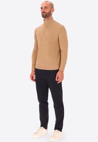 Maglione beige a collo alto realizzato in un morbido materiale knit, abbinato a pantaloni scuri e sneakers bianche. Design semplice, silhouette aderente.