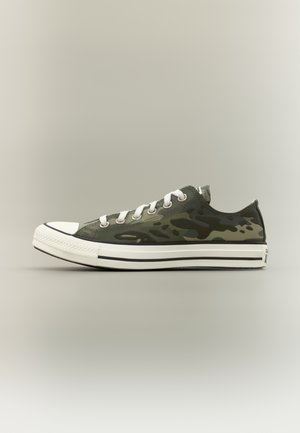 Low-top sneaker with green and black camouflage pattern, white laces, and white rubber sole with black stripes, shown in side profile.