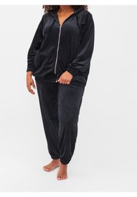 Černá semišová souprava tepláků obsahující mikinu na zip s tkanicemi a pružnými manžetami, doplněná o odpovídající zúžené kalhoty. Měkká textura.