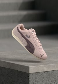 Sneaker rosa chiaro con dettagli mauve scuro, materiale scamosciato, pannello laterale testurizzato, suola bianca e logo Puma sul lato e sulla linguetta.