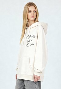 Felpa con cappuccio beige chiaro in tessuto morbido, con tasca frontale, cappuccio con coulisse e grafica nera di un uccello con la scritta "Liberté".