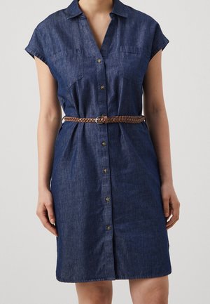 Vrouw draagt een donkerblauwe denim jurk met korte mouwen tot net boven de knie, met knopen aan de voorkant en een gevlochten bruine riem in de taille.