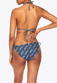 Bikini in denim con un motivo intrecciato nella parte inferiore. Lacci regolabili al collo e ai fianchi, con una texture liscia in blu navy.
