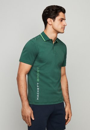 Polo shirt de algodón verde con una tapeta de dos botones, cuello amarillo en contraste y logo vertical "HACKETT SPORT" en blanco y verde en el lateral.