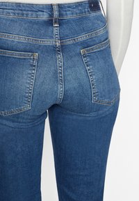 Mörkblå denimjeans med hög midja, bakfickor och subtil blekning. Har sömnadsdetaljer längs sömmarna och en mjuk textur.