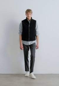 Fekete cipzáras mellény világosszürke ing felett, szürke nadrággal és fehér tornacipővel párosítva. Simogató tapintású anyag, tiszta vonalakkal és modern szabással.