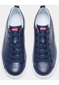 Adidași din piele bleumarin cu o finisare texturată, vârf rotund, talpă albă plată și șireturi albastre. Dispune de un eticheta logo roșie pe limbă.