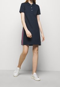 Marinblå poloklänning med korta ärmar, treknapplåst, och sidostråk i röd och vit. Stylar med vita sneakers.