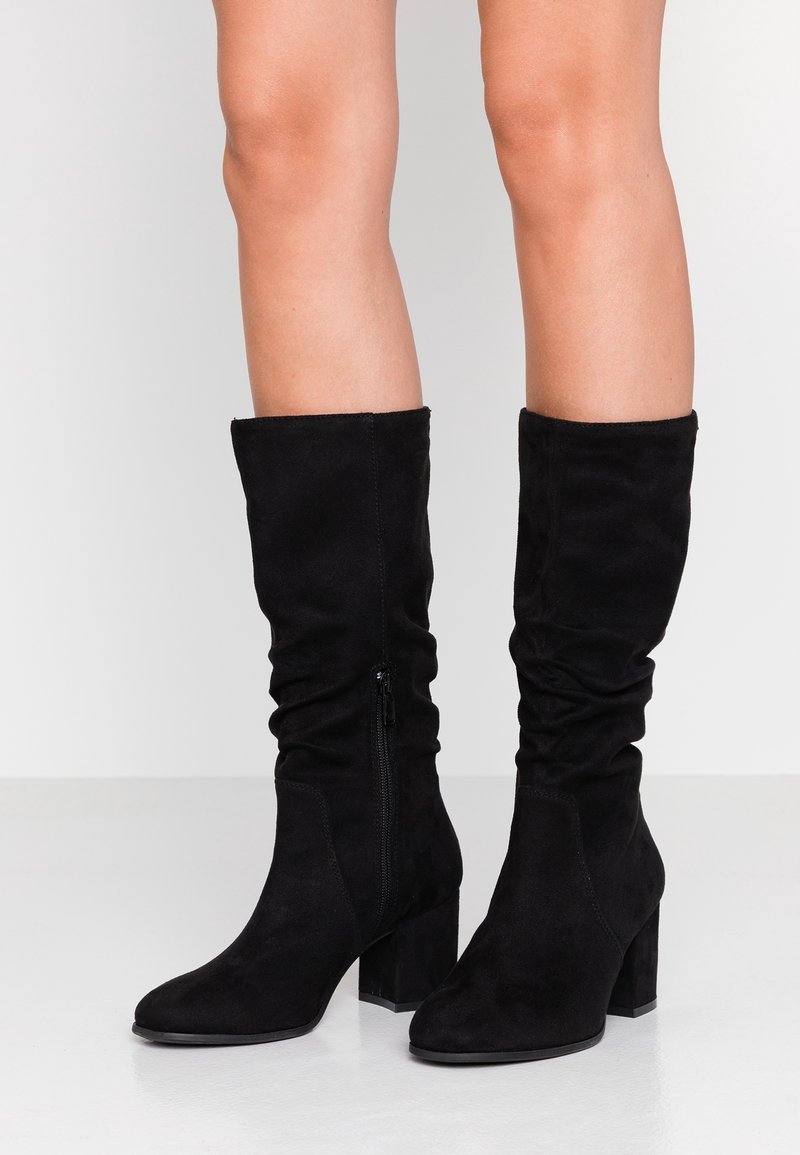 Svarta mocka knähöga stövlar med slouchy design, fyrkantig tå och 7,5 cm blockklack, med en sidodragkedja för enkel påtagning.