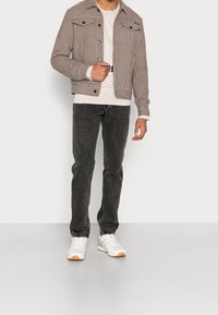 Brun och vit rutig jacka med framfickor, bärs över en ljusfärgad skjorta, kombinerad med mörka jeans och vita sneakers.