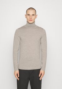 Beige coltrui gemaakt van zachte stof, aansluitend ontwerp met lange mouwen en een soepel textuur. Zwarte broek maakt de look compleet.