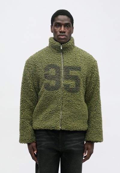Green fleece jacket with a high collar, zipper, and large black "95" printed on the front. Features a textured, soft surface.