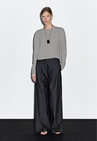 Gestreepte blouse met lange mouwen in zwart en wit, gecombineerd met hooggetailleerde, wijde donkergrijze broek. Bevat een eenvoudige zwarte hangerketting.