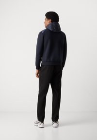 Navy sweatshirt with a quilted hood, paired with black pants and white sneakers, showcasing a modern, athletic design and textured accents.