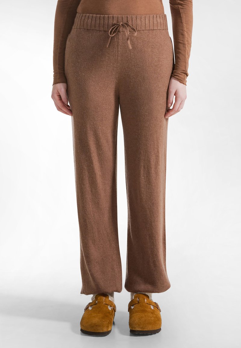 Bruine, wijde sweatpants met een geribde tailleband en trekkoord. Gemaakt van zachte stof, met een gladde textuur. Gecombineerd met bruine klompen.
