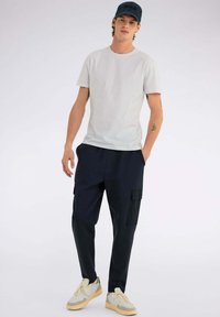 T-shirt grigio chiaro a maniche corte, pantaloni cargo blu navy con tasche laterali e sneakers beige con accenti verdi. Design semplice e funzionale.