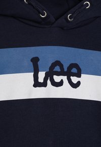 Námořnická mikina s světle modrými a bílými horizontálními pruhy, s vyšitým logem "Lee" v černé barvě na hrudi, s kapucí na šňůrku.