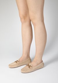 Semišové slip-on mokasíny v béžové barvě se šitým designem, dekorativním kovovým kováním vpředu a gumovou podrážkou pro lepší přilnavost.