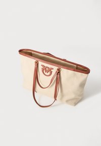 Canvas tote bag in crèmekleur met bruine leren accenten. Beschikt over dubbele handgrepen en een reliëflogo aan de voorkant. Open ontwerp aan de bovenkant.