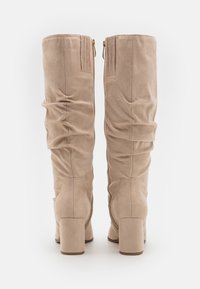 Stivali beige in suede al ginocchio con design arricciato, tacco a blocco e dettagli in zip dorati sul retro. Texture liscia con cuciture visibili.