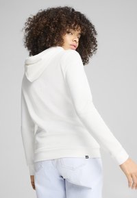 Sudadera blanca hecha de un tejido suave, con capucha, mangas largas y puños acanalados. Combinada con jeans de mezclilla azul claro.