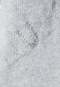 Grauer Strickpullover mit strukturiertem Muster und verziert mit silberfarbenen Strasssteinen, die den Buchstaben "U" bilden.