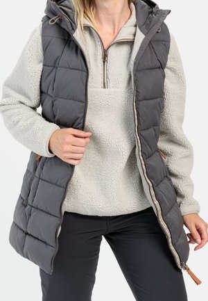 Grijze puffer vest met een gewatteerd ontwerp, ritssluiting en capuchon, gelaagd over een lichte fleece pullover. Gestyled met zwarte broek.