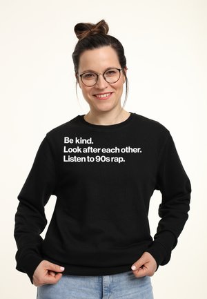 Sweatshirt noir à manches longues et col rond, avec un texte blanc : "Soyez gentils. Prenez soin les uns des autres. Écoutez du rap des années 90."