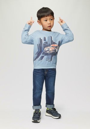 Lichtblauwe sweatshirt met lange mouwen, versierd met een stadsgezicht en voertuigprint, gecombineerd met donkerblauwe spijkerbroek en zwarte sneakers.