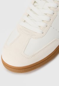 Witte leren en suède sneaker met een gumrubberen zool, voorzien van witte veters en geperforeerde accenten op de neus.