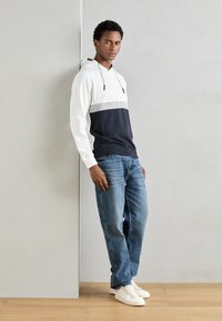 Felpa con cappuccio con blocchi bianchi, grigi e blu navy; tessuto misto cotone. Abbinata a jeans blu sbiaditi e scarpe da ginnastica bianche.