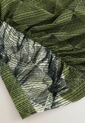 Texturerat tyg i mörkgrönt och krämvitt med svarta geometriska mönster. Har veckade kanter och ett skrynkligt ytskikt.