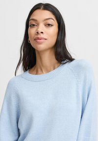 Světle modrý svetr s kulatým výstřihem a žebrovanými manžetami, s jemnou texturou a subtilními pletenými detaily na ramenou.