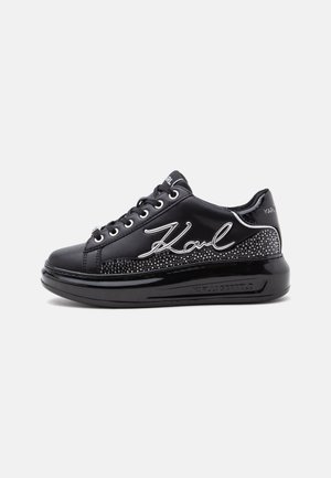 Baskets basses noires avec lacets noirs, semelle brillante, panneau latéral clouté et signature "Karl" en blanc sur le côté extérieur.