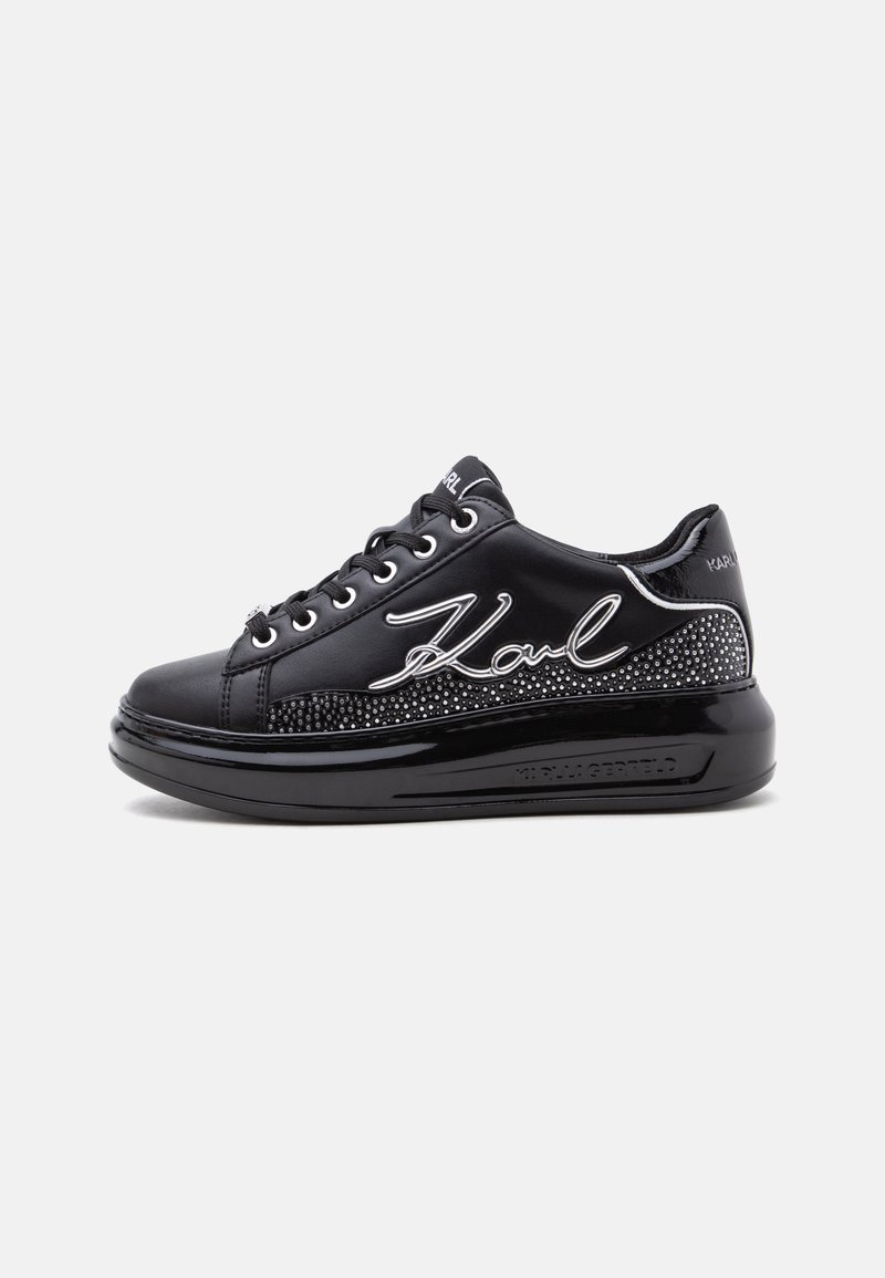 Μαύρο sneaker χαμηλού τύπου με μαύρα κορδόνια, γυαλιστερή σόλα, πλευρικό πάνελ με καρφιά και λευκή υπογραφή "Karl" στην εξωτερική πλευρά.