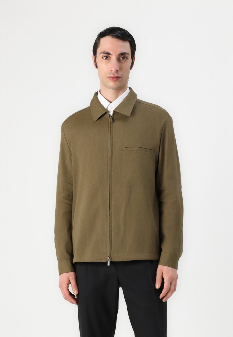 Rudas zip-up striukė su apykakle, viena krūtinės kišenė ir ilgomis rankovėmis. Lygi tekstūra, lengvas audinys ir minimalistinis dizainas.