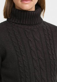 Pull à col roulé en tricot gris foncé avec un motif de cables texturé et un col côtelé, fabriqué à partir d'un mélange de laine épais et chaud.
