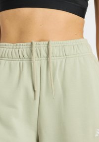 Light green sweatpants feature an elastic waistband with a drawstring, with a soft texture and subtle stitching details.