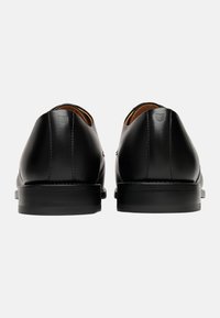 Chaussures en cuir noir avec une finition lisse, bout rond et design minimaliste. Semelle plate en caoutchouc noir et accents de couture discrets.