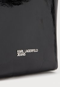 Bolsa preta e brilhante feita de material sintético. Apresenta um logótipo prateado que diz "KARL LAGERFELD JEANS" na parte da frente.