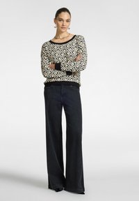 Suéter de canalé negro y crema con un patrón de diamantes geométricos, cuello redondo y puños acanalados, combinado con jeans de mezclilla oscuros de pierna ancha.
