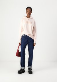 Svetlo roza hudica z logotipom "Calvin Klein", temno modri džins s zavitimi manšetami, črne platform čevlje in mala rdeča torbica.