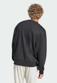 Sort sweatshirt med en afslappet pasform, bred udskæring og ribbede manchetter, parret med lyse bukser; blød tekstur og minimalistisk design.