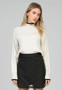 Pull en maille blanche avec un col haut, associé à une jupe noire à rayures avec un ourlet en dentelle. Le tissu semble doux avec des côtes et une texture visibles.
