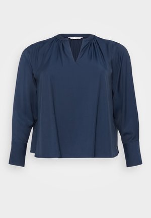Tums zila garām piedurknēm blūze ar V veida kakla izgriezumu, mīksta auduma, ar saliktām plecu detaļām un aprocēm uz piedurknēm. Vienkārša un brīva piegriezuma.