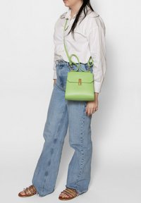 Groene leren handtas met een klepsluiting, gouden hardware en een afneembare schouderband. Draagt bij hoge taille blauwe jeans.