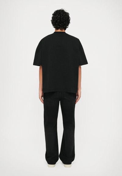 Zwarte oversized t-shirt met korte mouwen, gecombineerd met zwarte flared jeans en lichtgekleurde sneakers, gezien vanuit de achterkant.