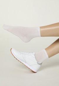 Zapato deportivo blanco con detalles en gris, combinado con calcetines acanalados de color rosa claro. Enfoque en la textura suave del cuero del zapato y la suela de goma.