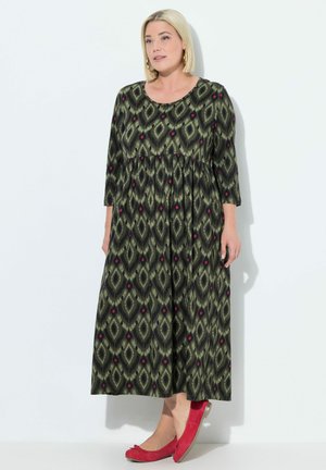Robe maxi de couleur vert foncé avec un motif en losange, ornée d'accents roses. Manches longues, col rond et taille froncée. Accompagnée de ballerines rouges.