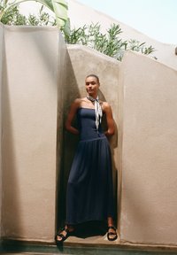 Navy-blaues, trägerloses Maxikleid aus strukturiertem Stoff, mit passgenauem Oberteil und fließendem Rock. Akzentuiert mit einem schwarz-weißen gemusterten Schal.